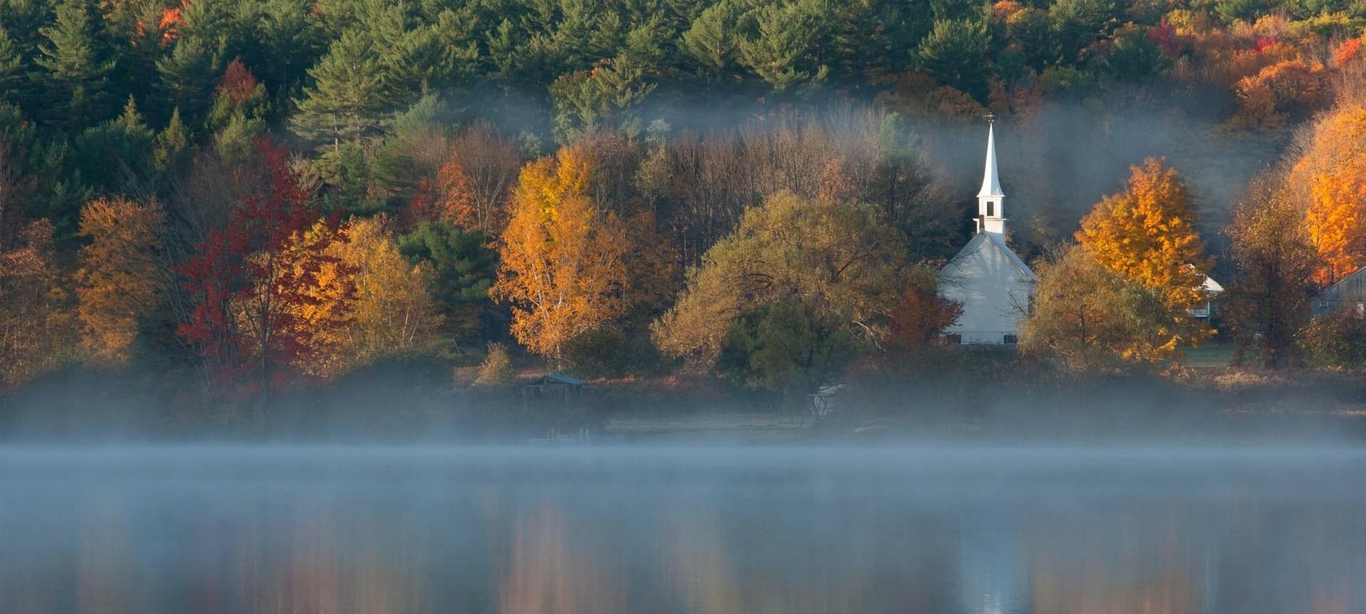 Church with steeple surrounded by trees and a lake