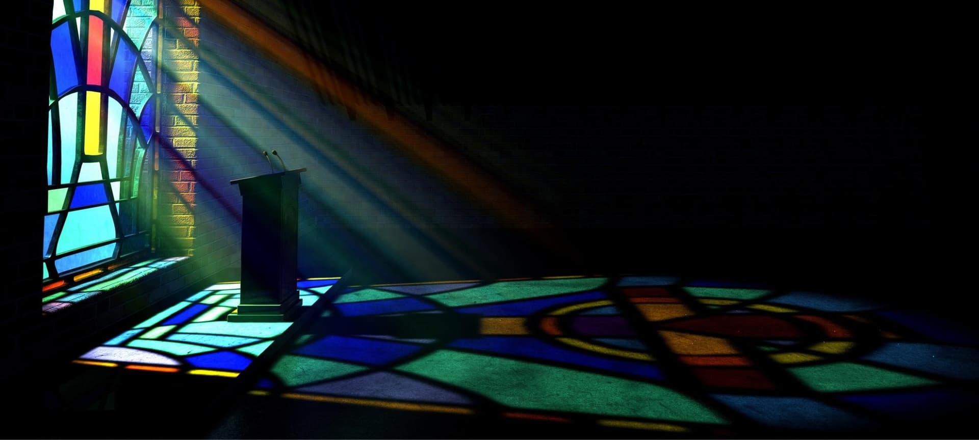 Empty dark church with light shining through faintly through stained glass window