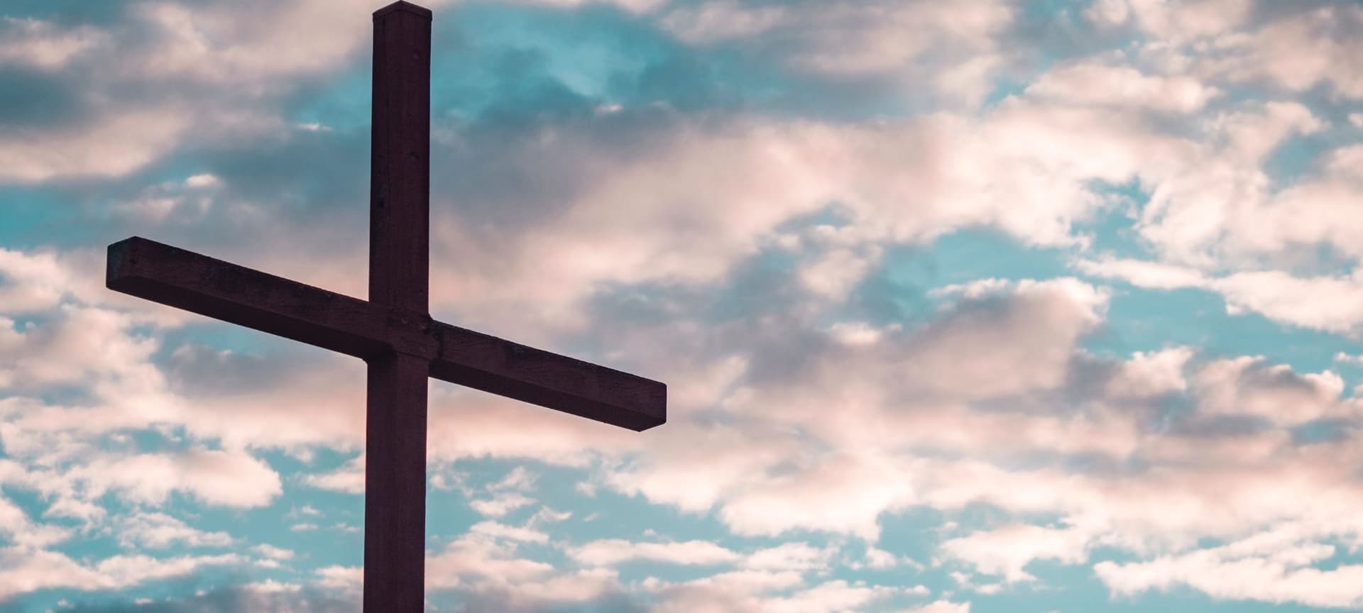 A cross with a sky full of clouds behind it