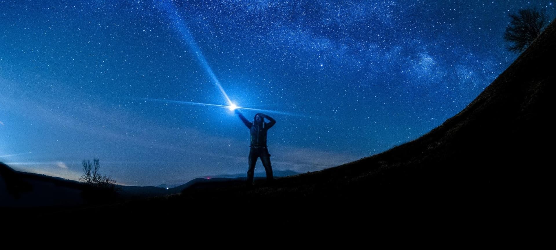 Blue night sky with stars and person holding flashlight upwards