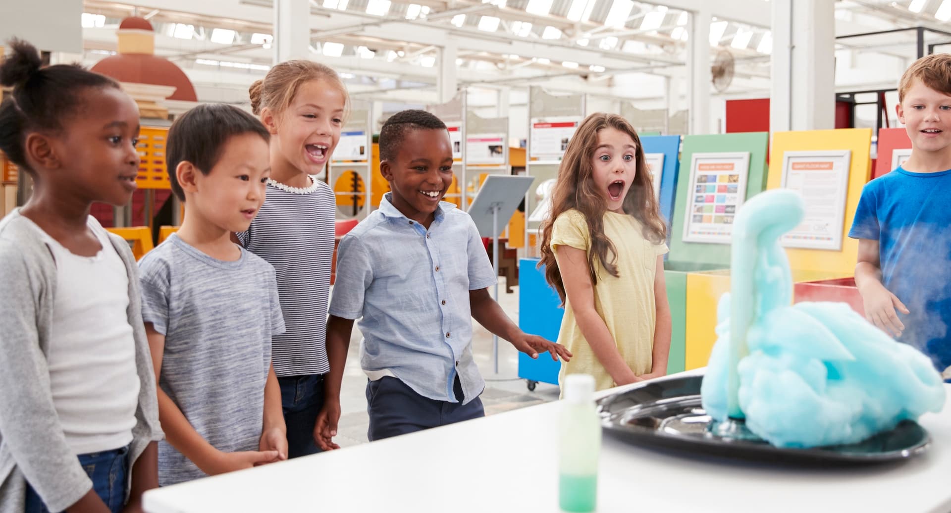 kids around a table that has a blue foamy science experiment occurring