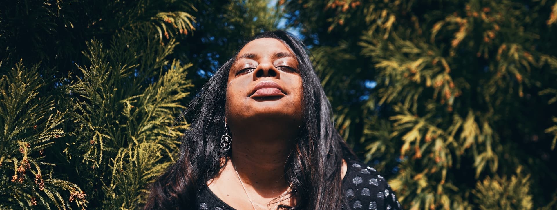 woman in a pine forest with her face raised to the sun with her eyes closed