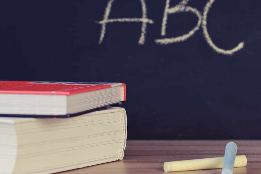 two books on a table with two pieces of chalk with a chalkboard in the background