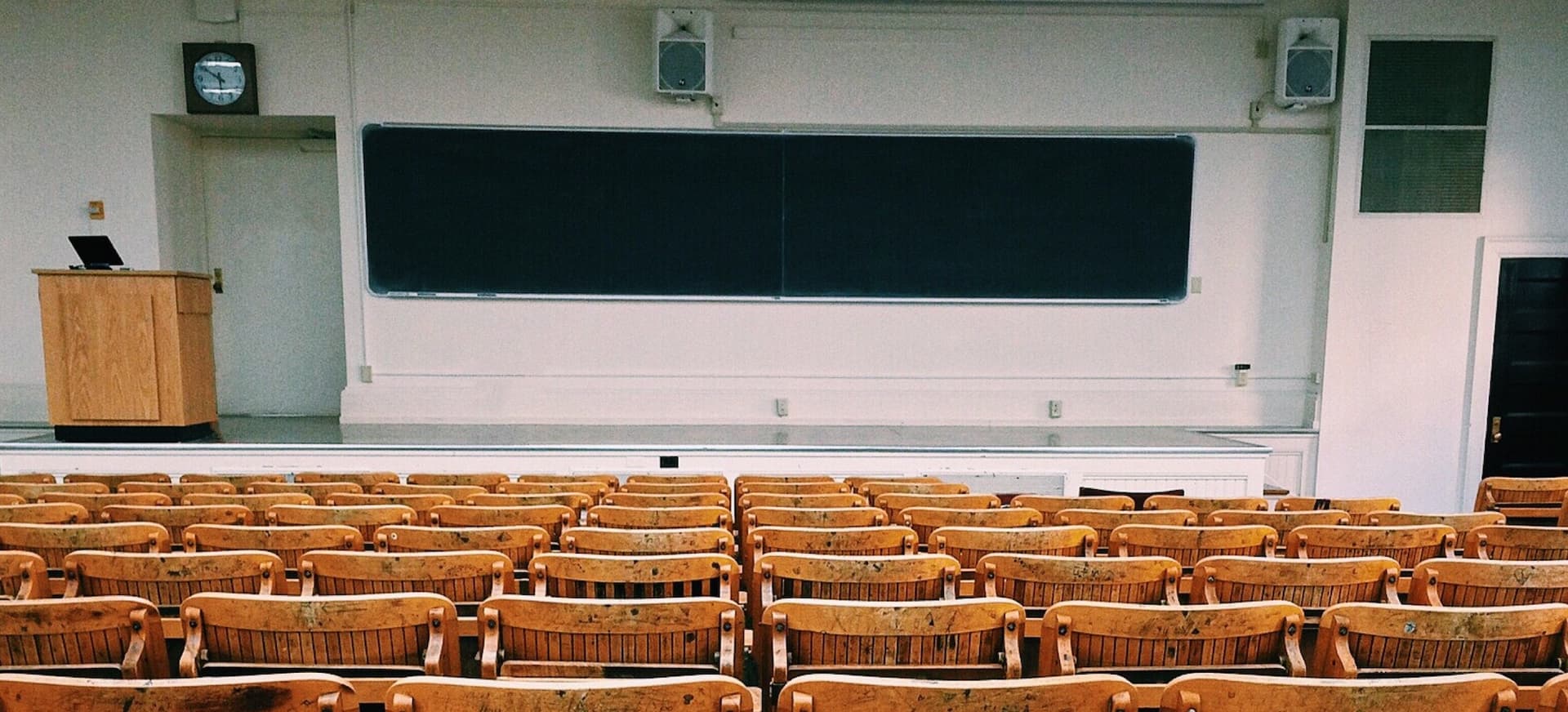 an empty lecture style classroom with a black chalkboard at the front