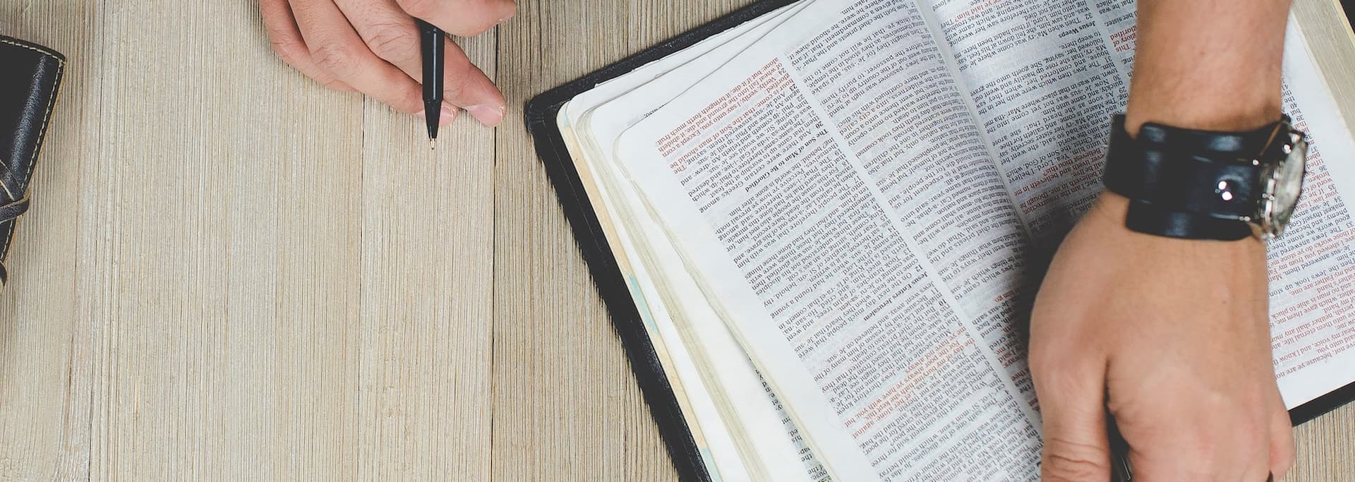 man's hands holding a bible and pen on a table