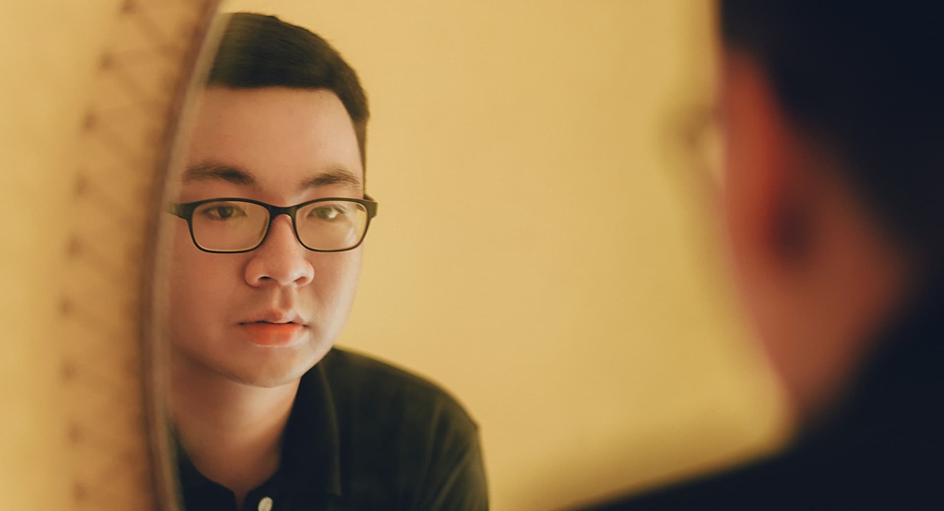 man in glasses looks into a mirror