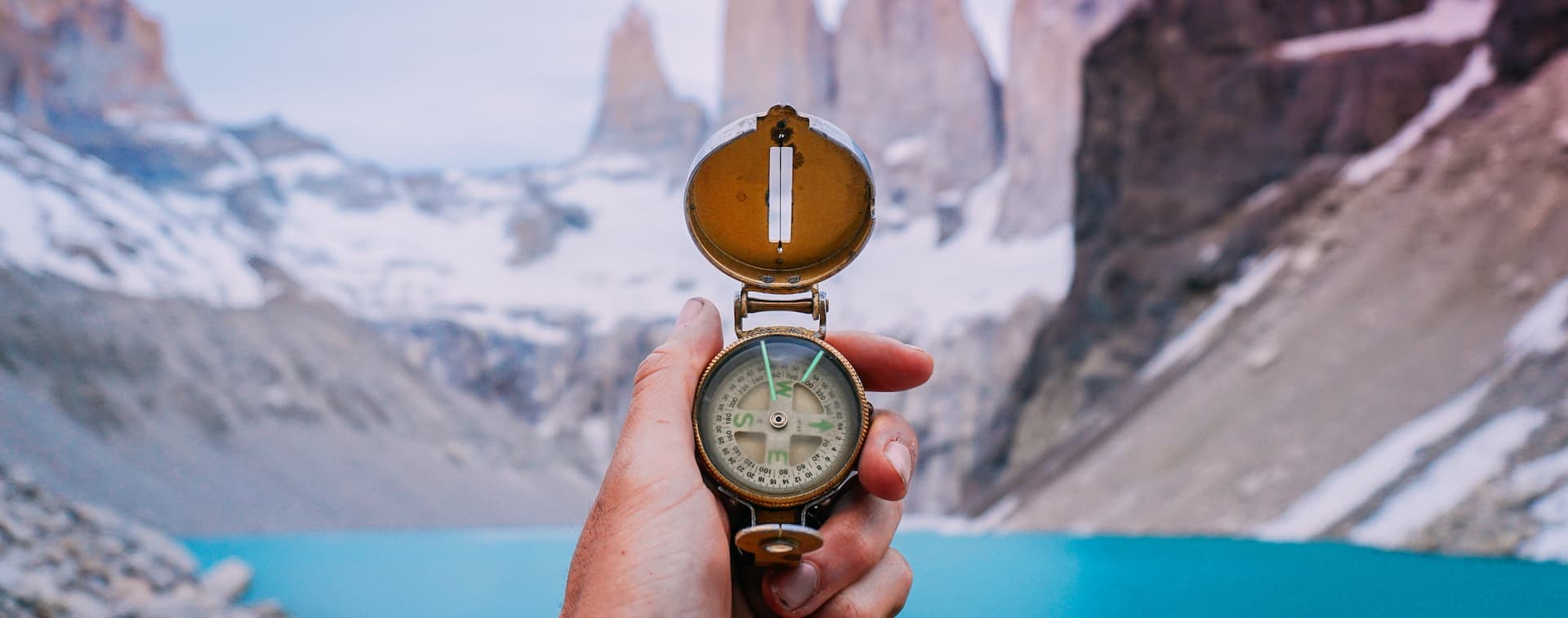 hand holding compass over blue lake and mountains