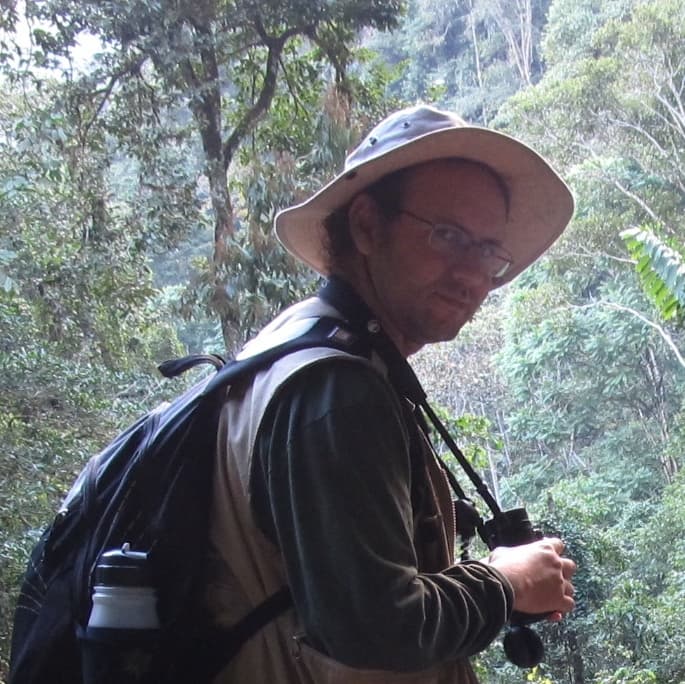 Oscar Gonzalez in a jungle doing fieldwork with binoculars