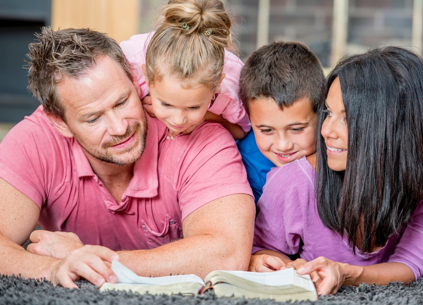 family of four reading a bible on the ground