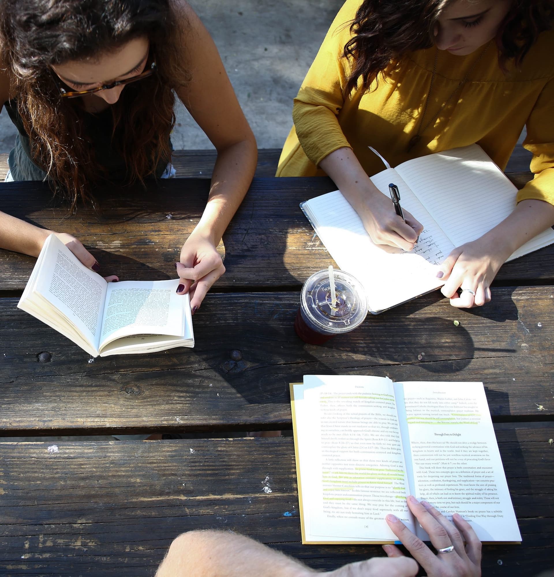 three people reading open books at a table