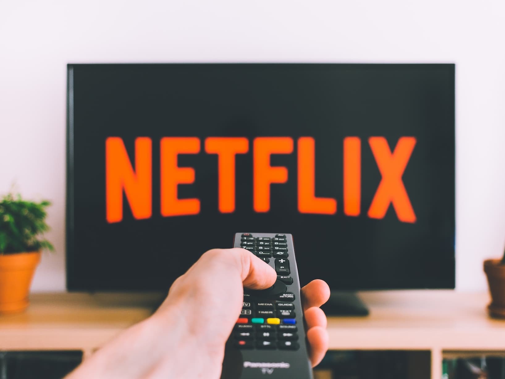 Netflix logo on a TV with a hand and a remote in the foreground
