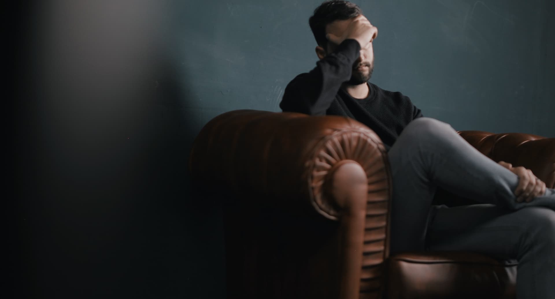 man covering face and sitting on a couch
