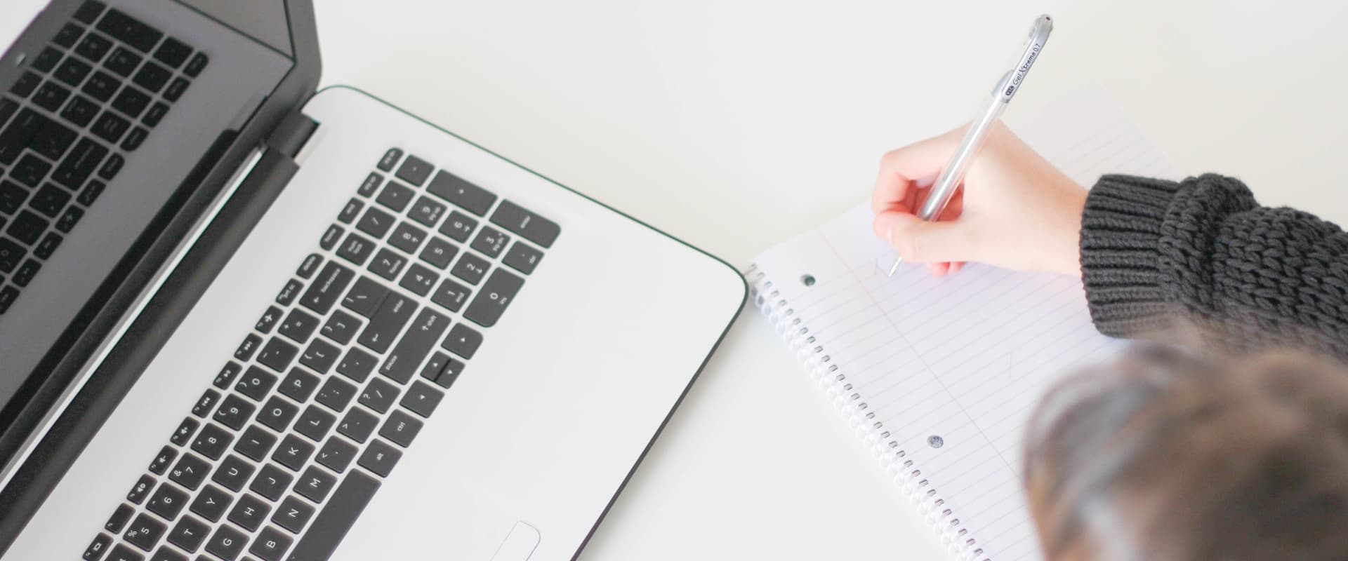girl writing in a notebook by an open laptop