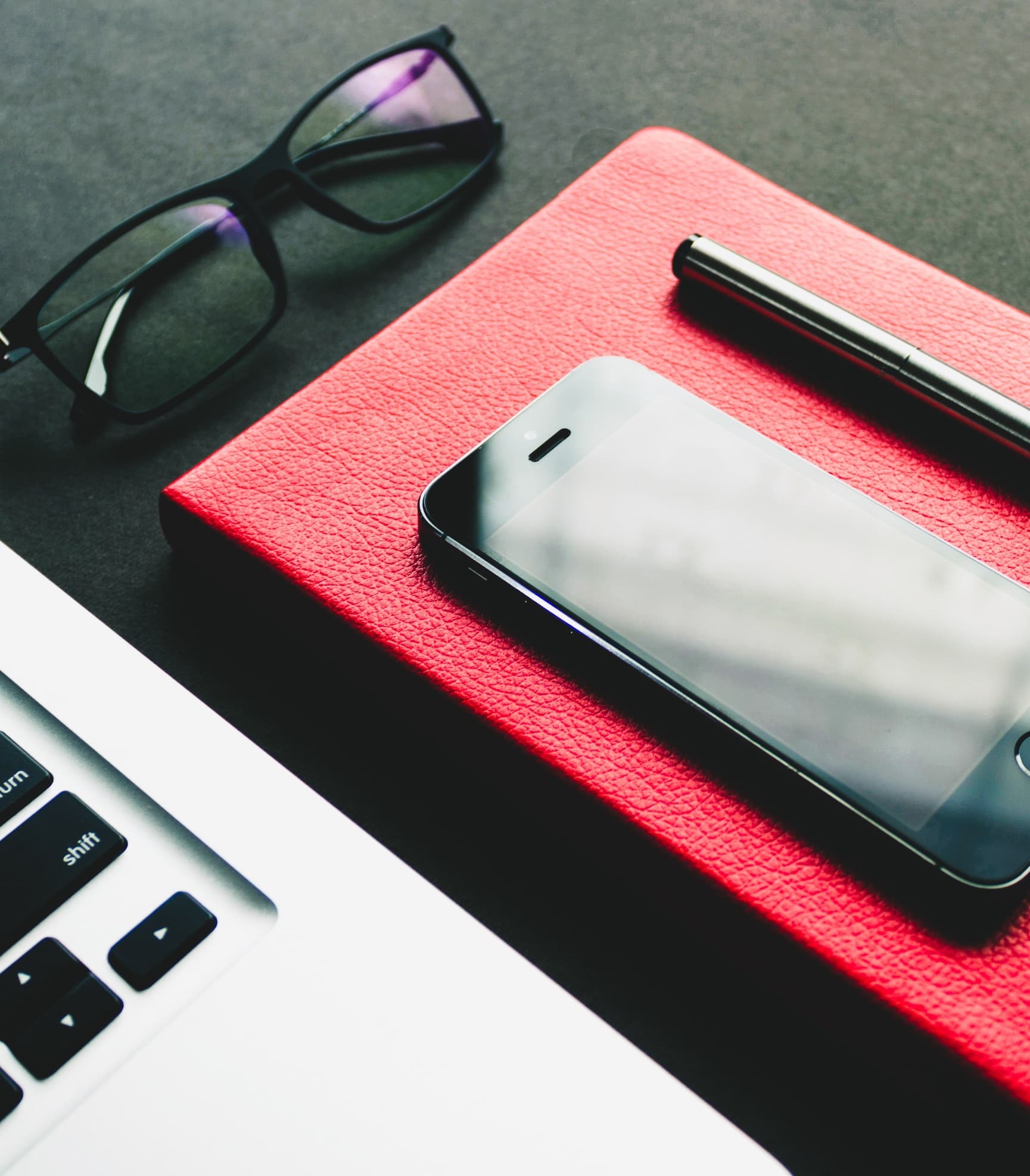 phone and pen on top of notebook, sitting next to an open laptop and glasses