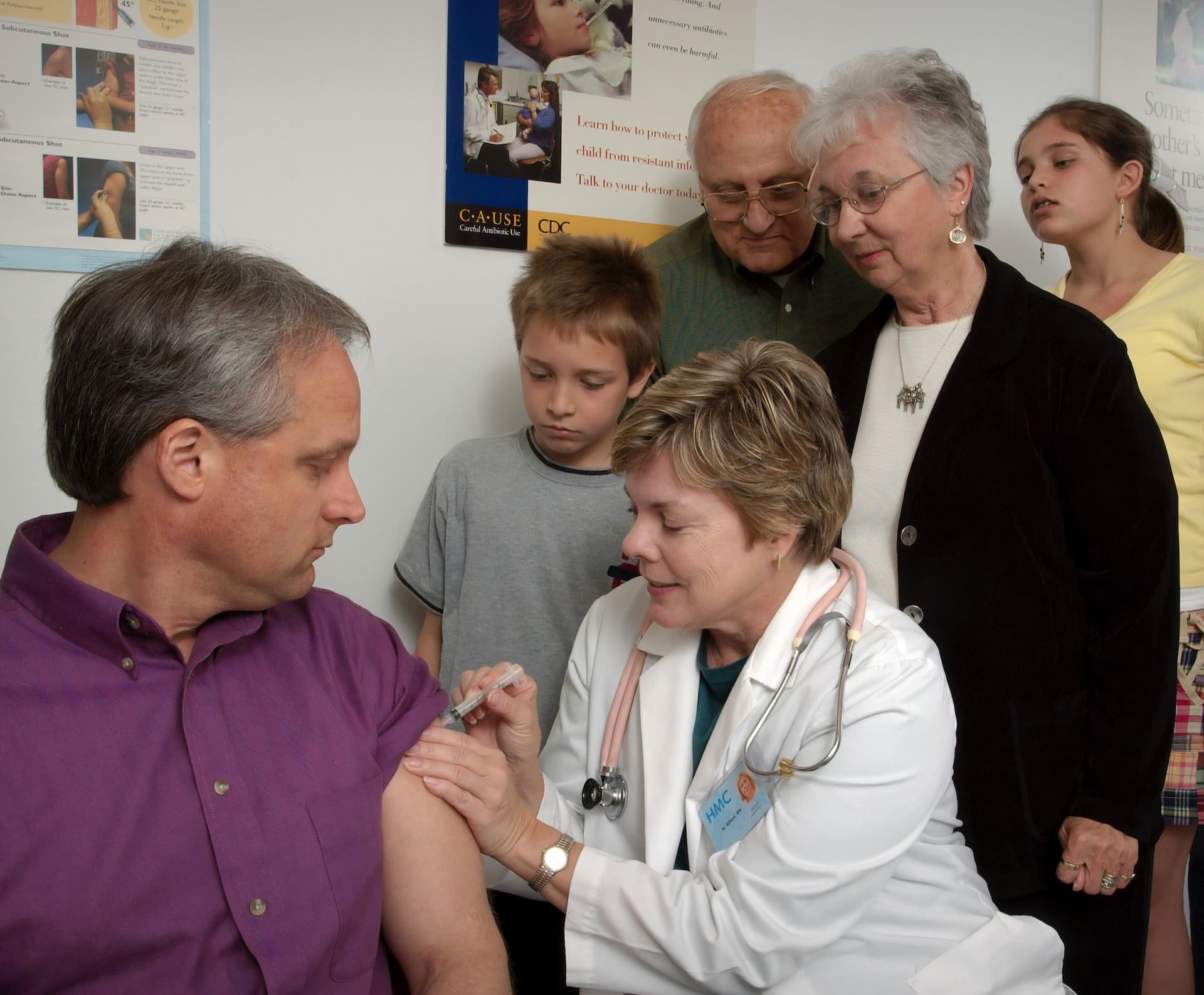 a woman giving a vaccine to a man while 4 other people look on