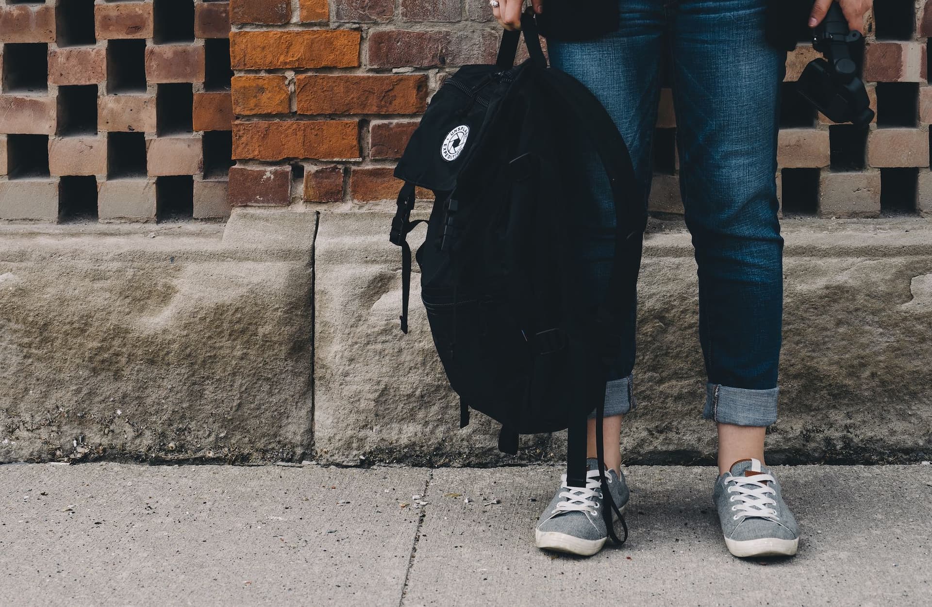 a person's legs standing on a sidewalk, holding a backpack