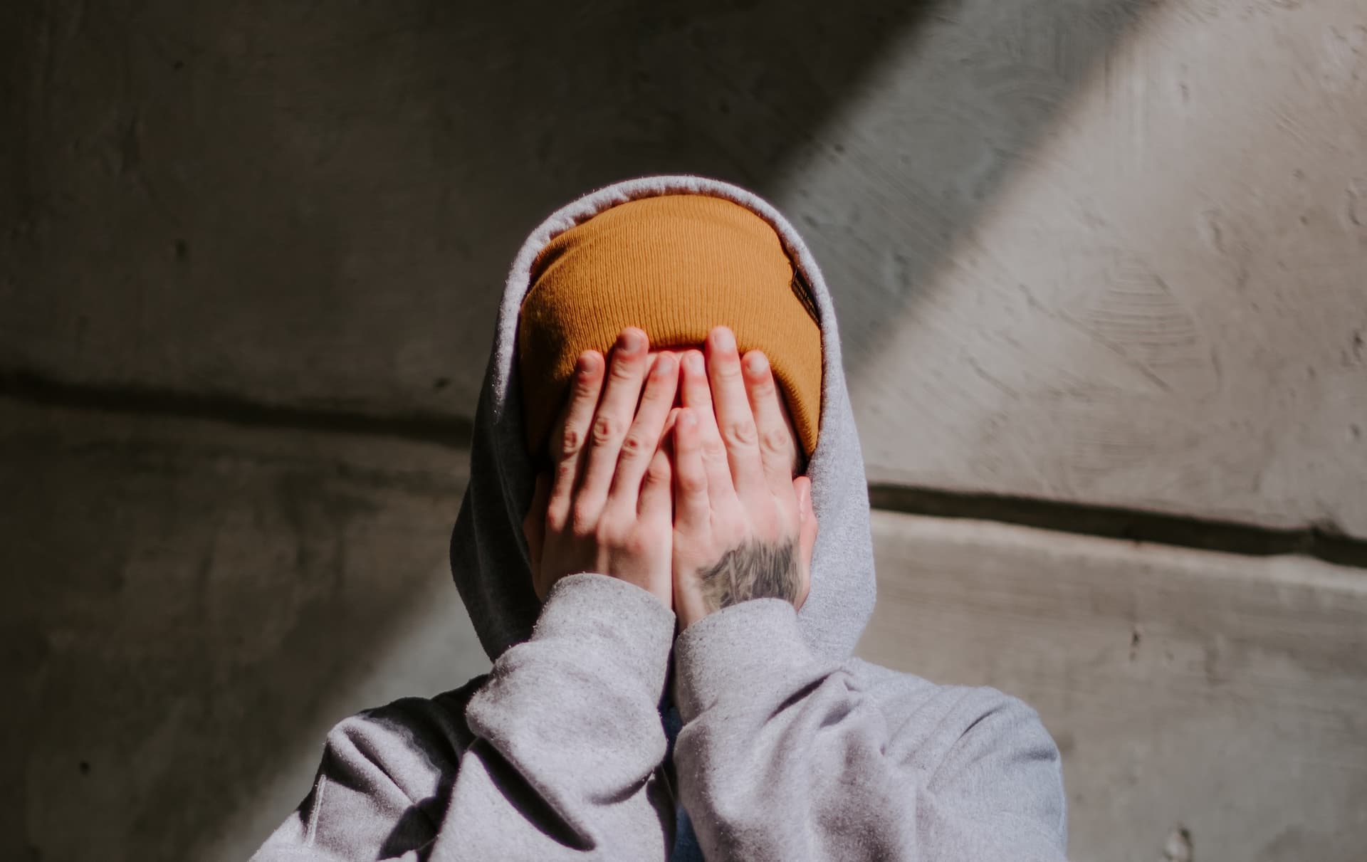 person in yellow beanie and gray hoodie covering face with hands