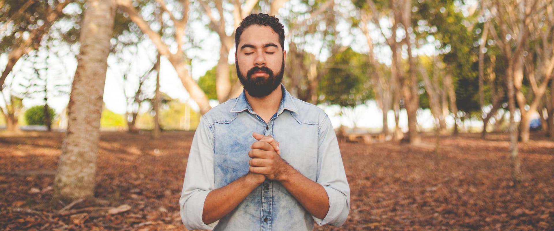 man standing praying in the woods