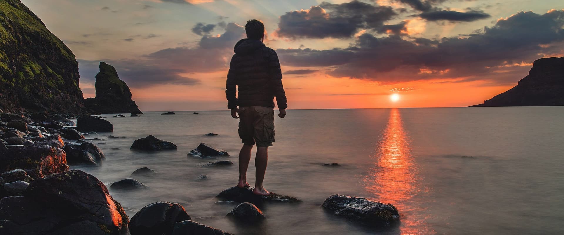 silhouette of person standing on rock in water looking at sunset
