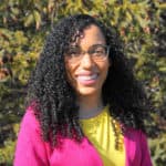 Photo of Veronica Frans. Veronica is smiling while standing in front of an evergreen tree.