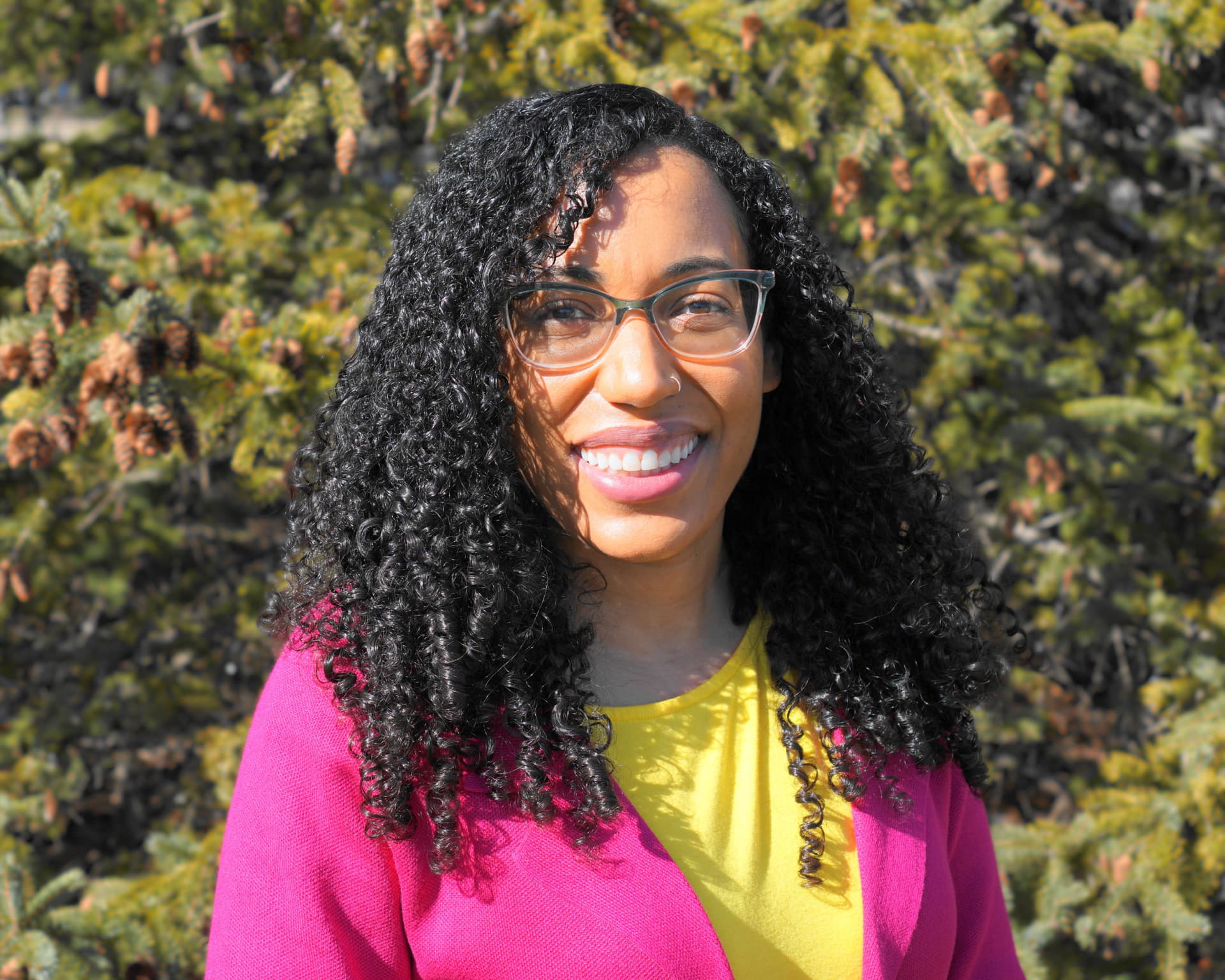 Photo of Veronica Frans. Veronica is smiling while standing in front of an evergreen tree.