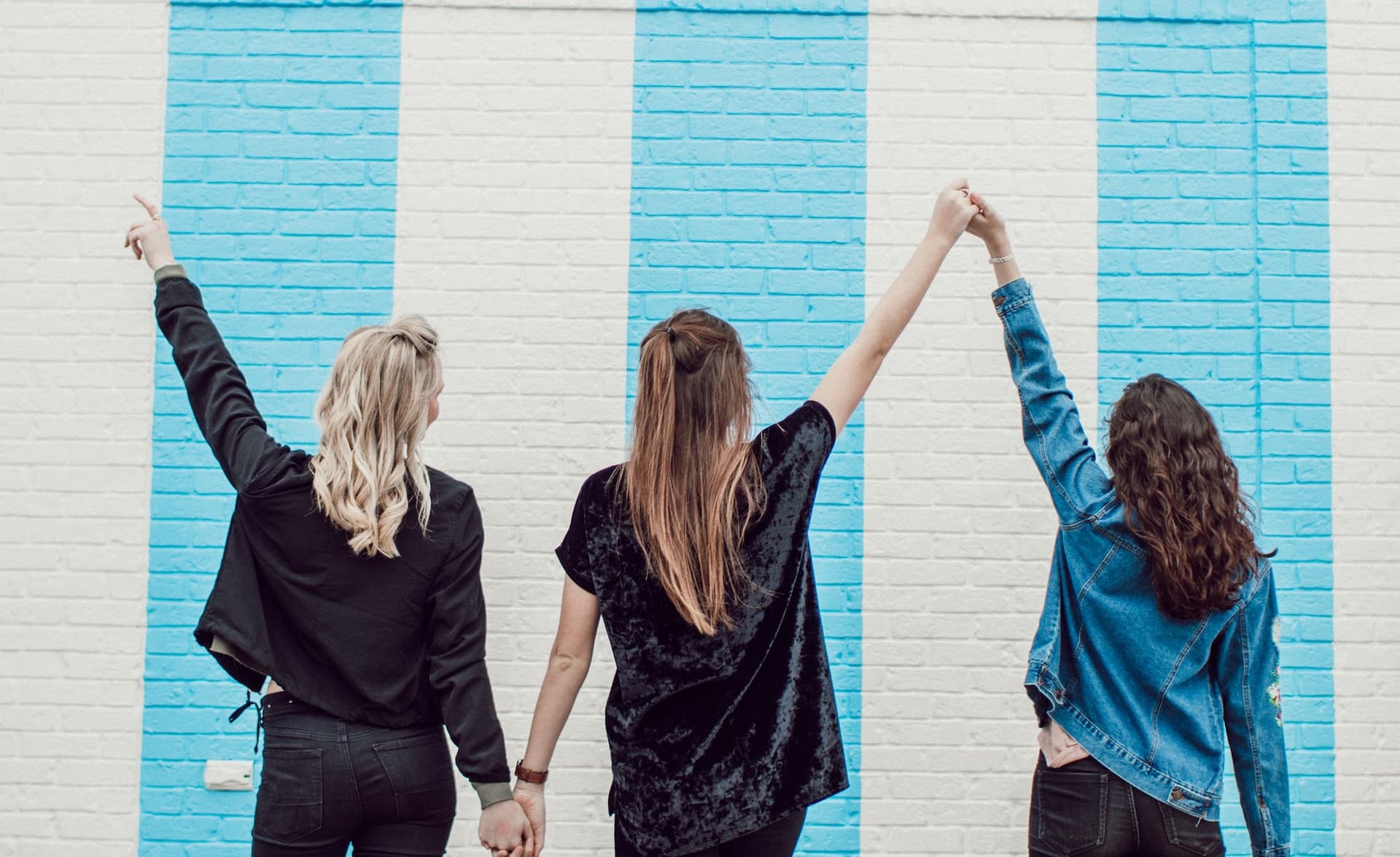 the backs of three women, holding hands facing a wall