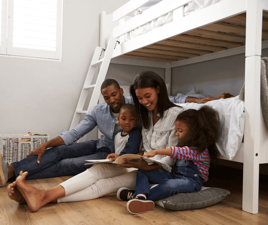 family of two parents and two kids reading a book while leaned up against a bunk bed