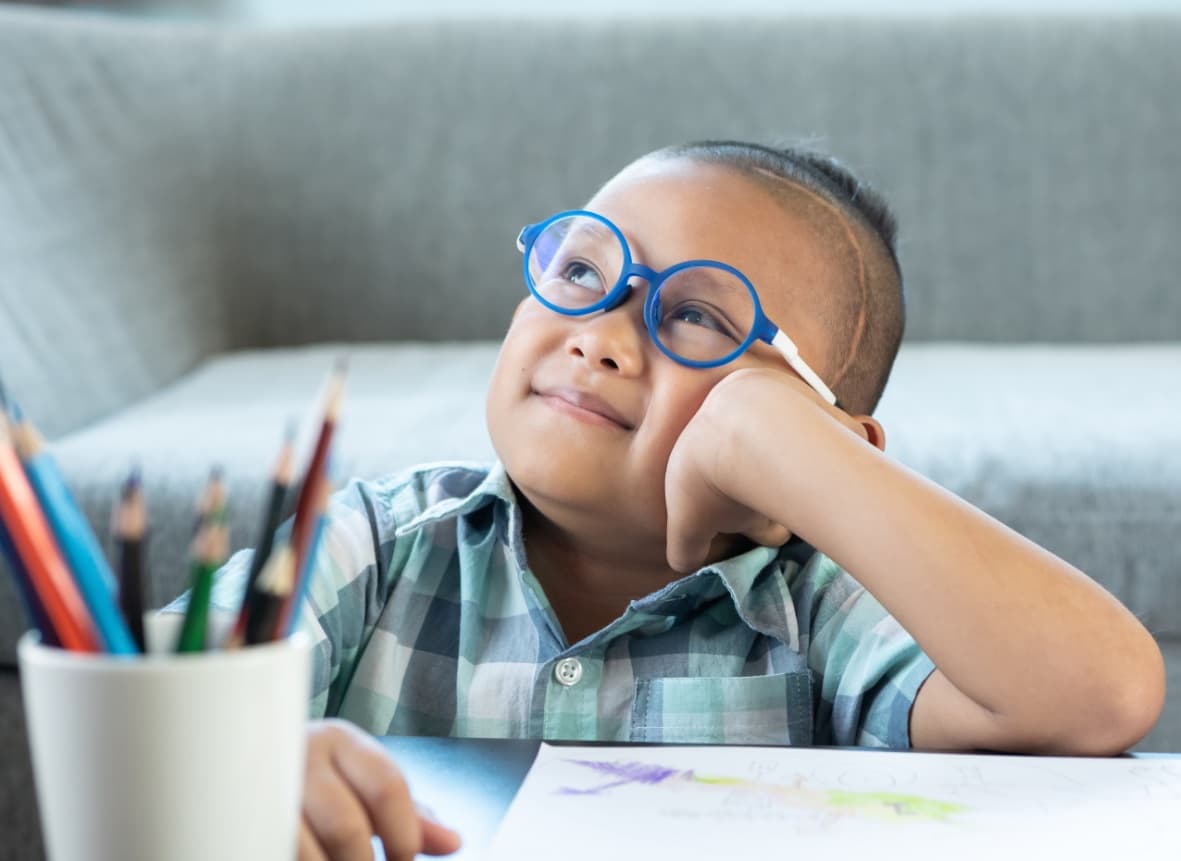 child in glasses looking into space while drawing