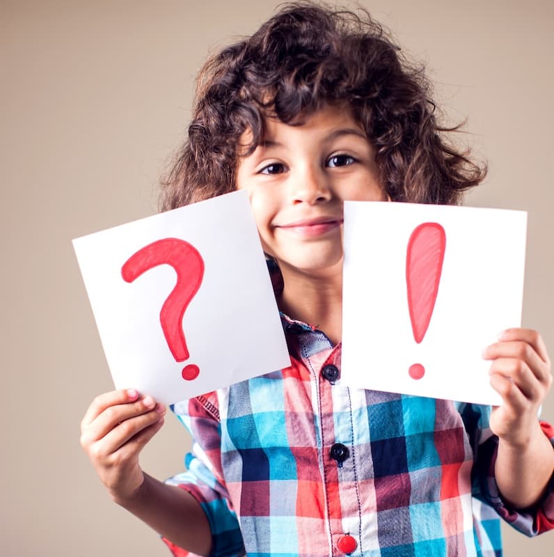 child holding two pieces of paper, one with an exclamation point and the other a question mark on it