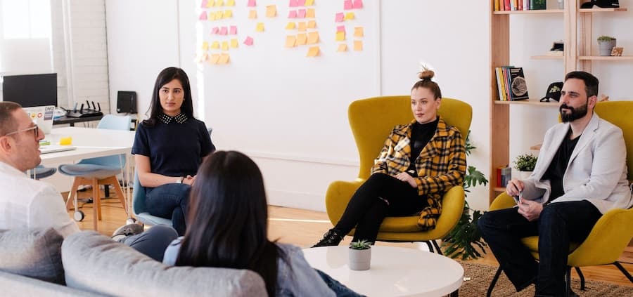 people sitting in chairs in a circle around a coffee table talking