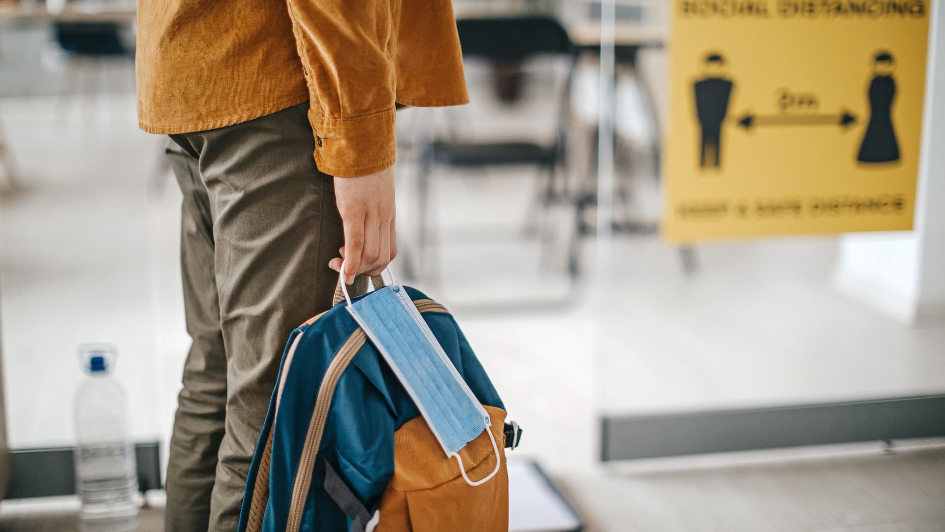 Student holds mask with school bag