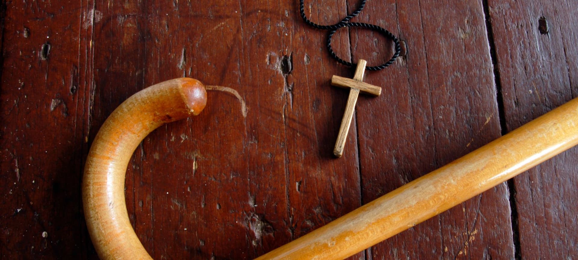 A cross necklace side by side a wooden cane
