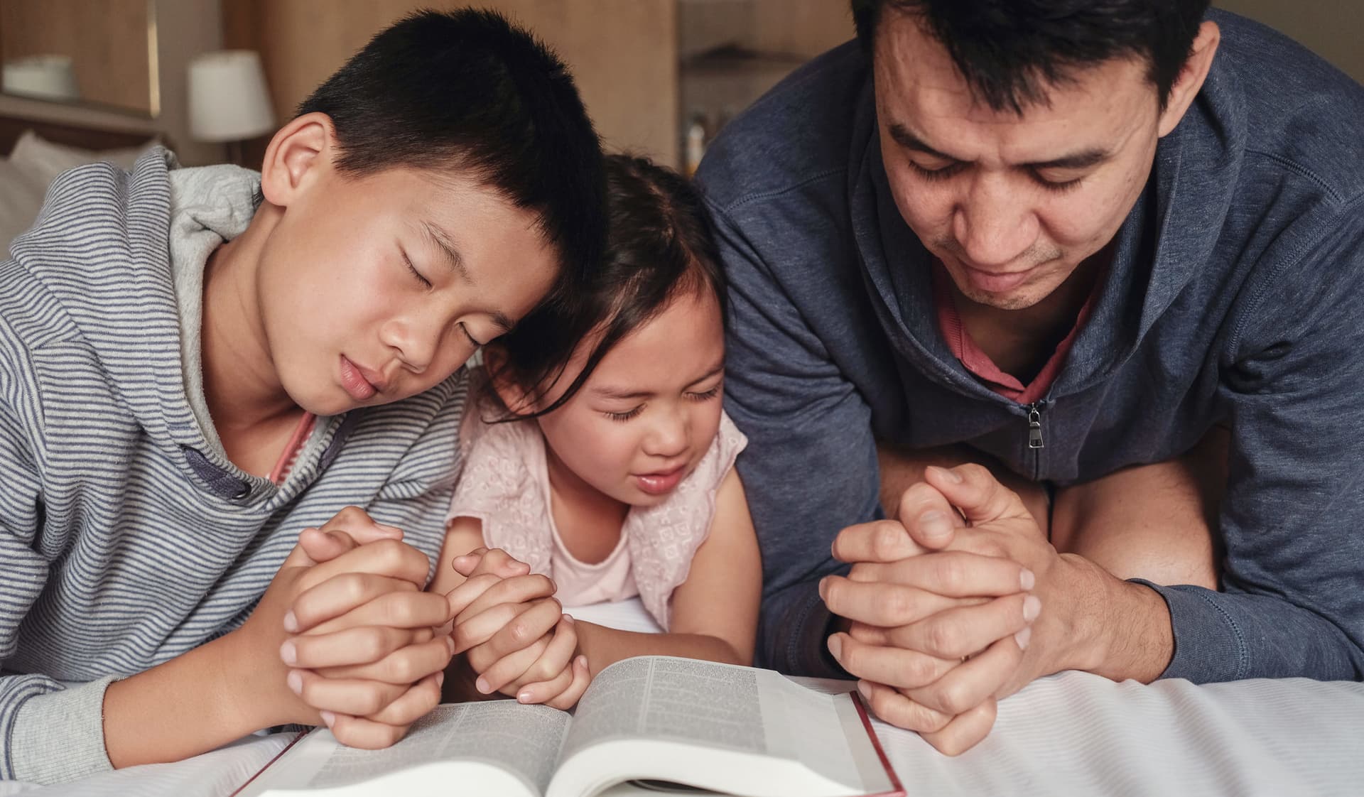 Children with parent praying and reading the bible