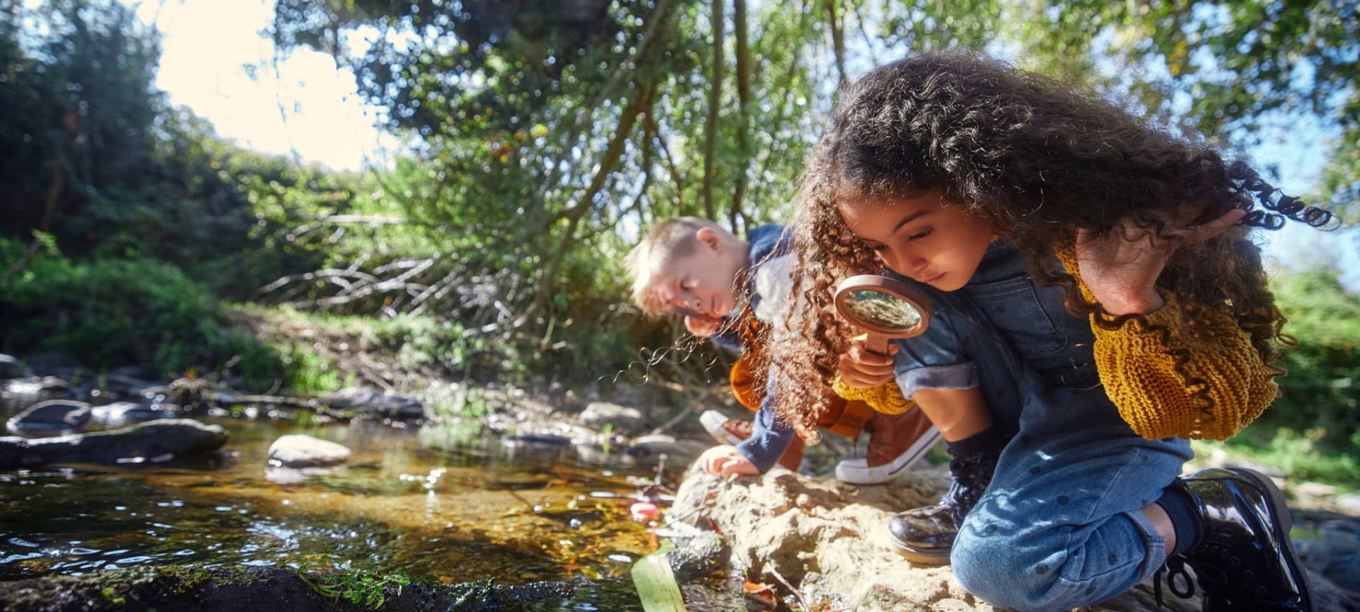Kids looking closely at stream of water using magnifying glass