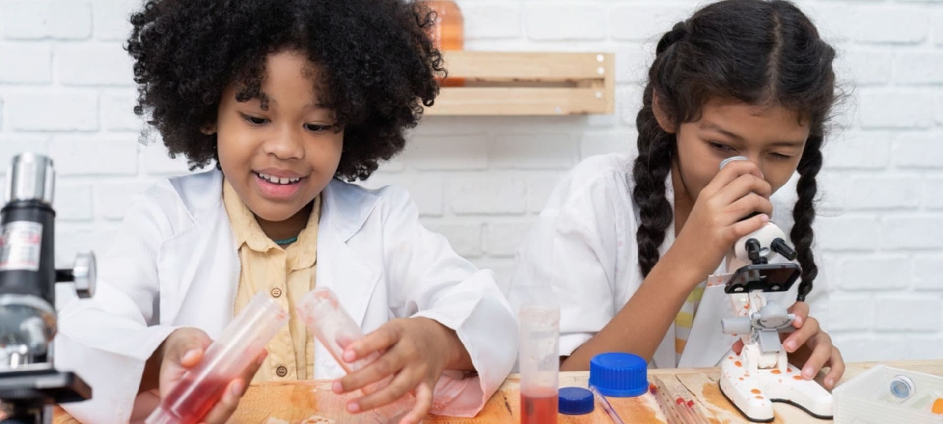 Two children having fun experimenting in a lab, one with liquids, the other looking through a microscope