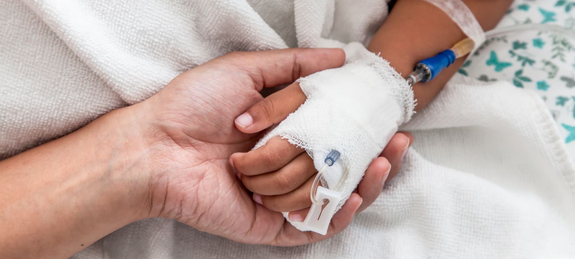 Adult hand embracing child's hand who has an IV
