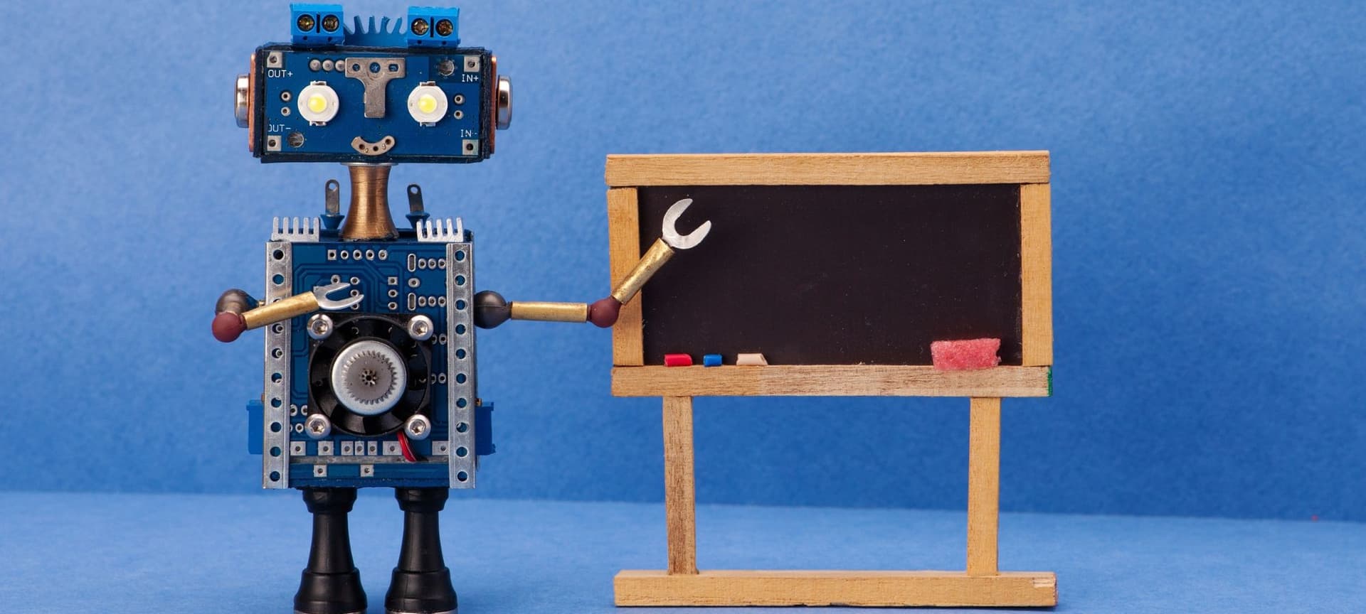 An adorable toy robot standing in front of a blackboard as if teaching a class