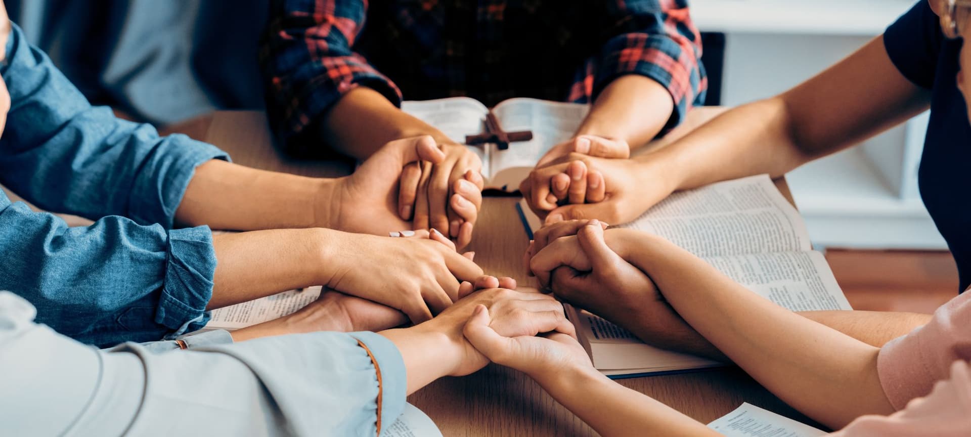 People holding hands and praying with bibles open.
