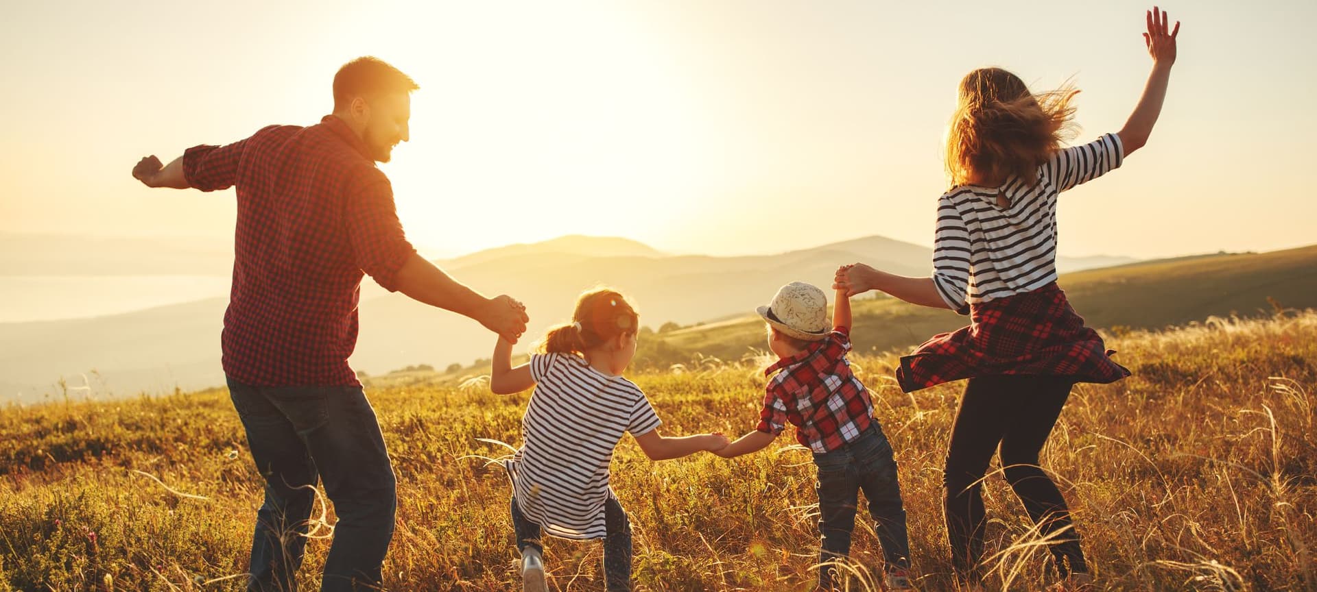 A family holding hands and running through the grass towards the sun during a sunset in a joyful mood.