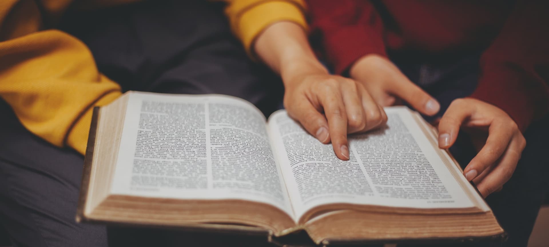 Closeup of two people reading an open bible, with one person's hand pointing to a passage.
