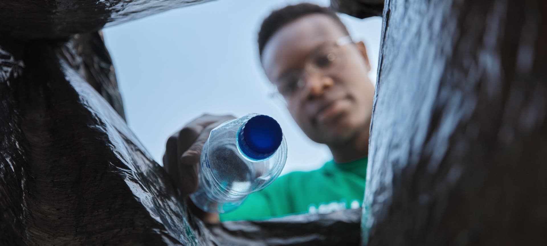 Closeup of person placing a plastic bottle in a trash bag. view is from underneath, as though looking up from the bottom of the trash bag.