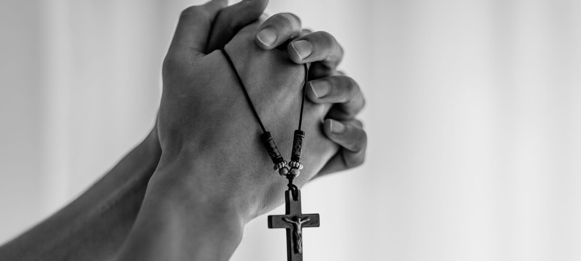 Closed prayer hands holding a rosary.