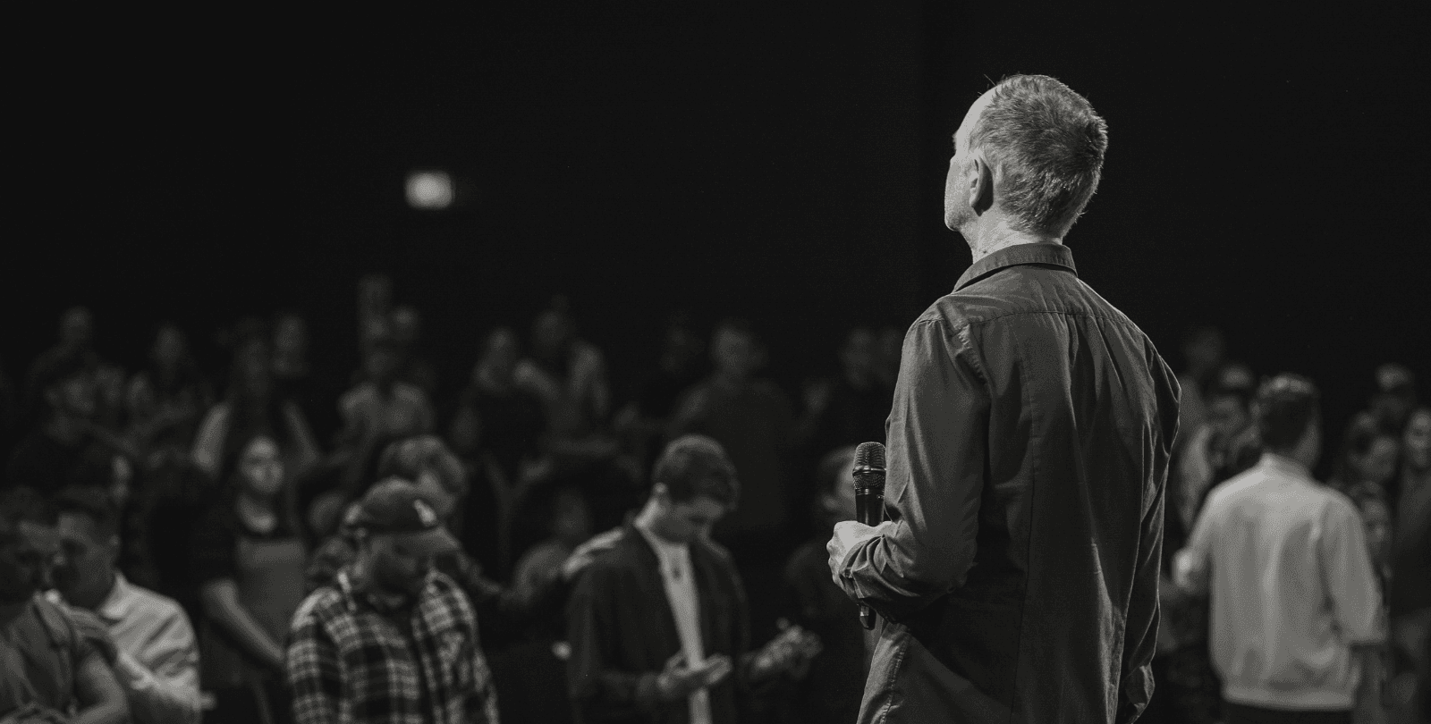 A pastor speaks to his congregation. Members of the congregation bow their heads in prayer.