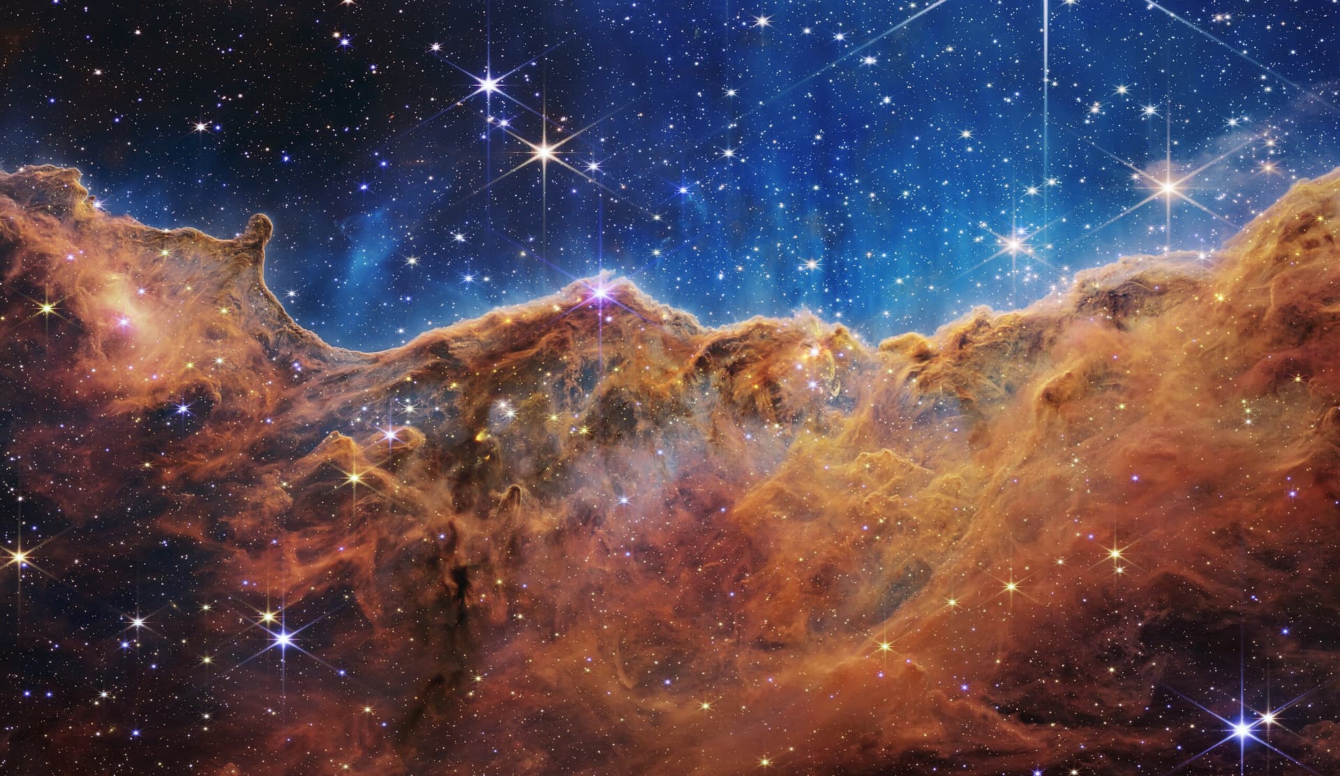 An image of the Carina Nebula's "Cosmic Cliffs," taken by the James Webb Space Telescope. Hundreds of galaxies shine in space.