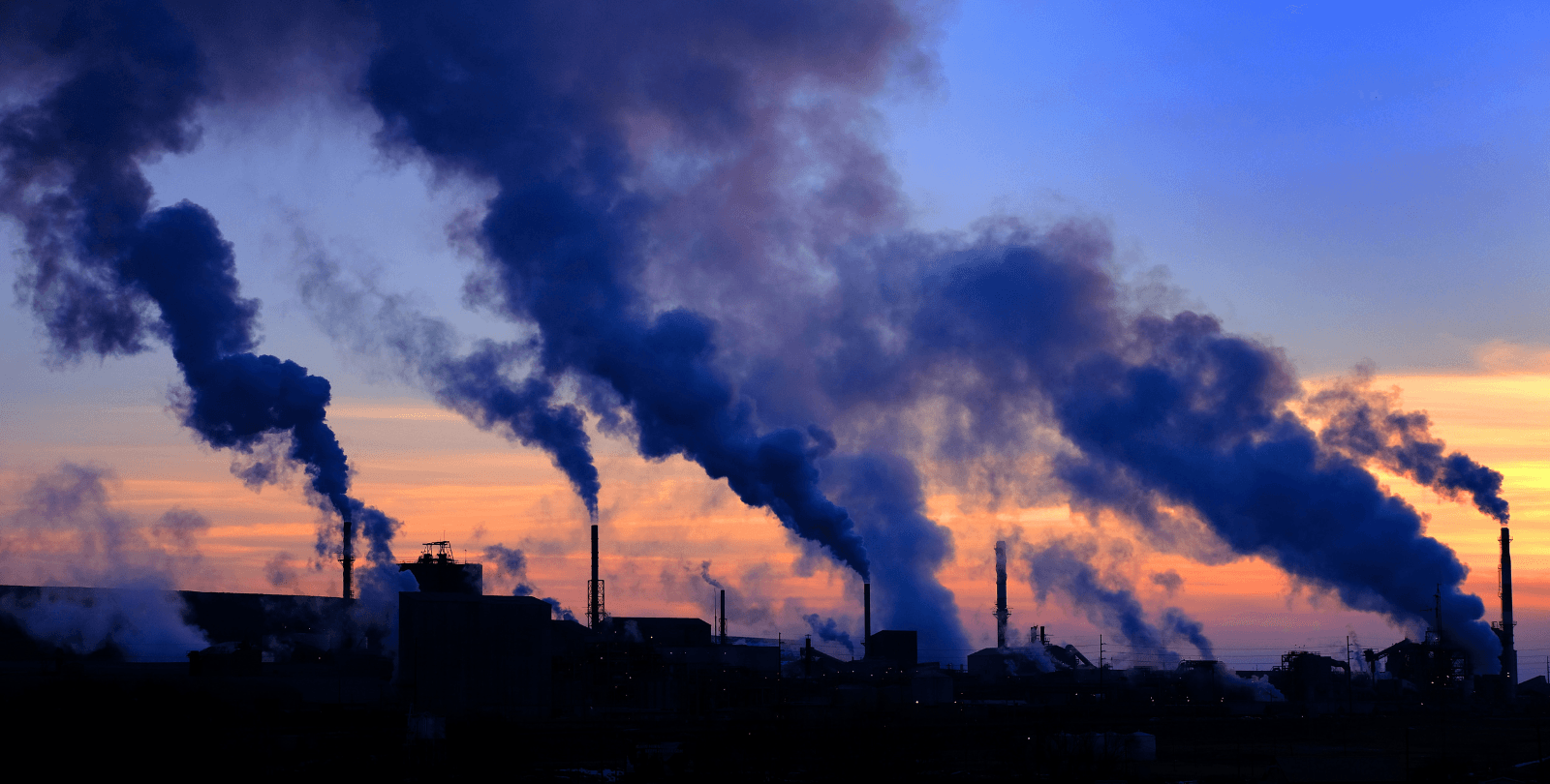 Smokestacks spew clouds of smoke into the sky at dusk.