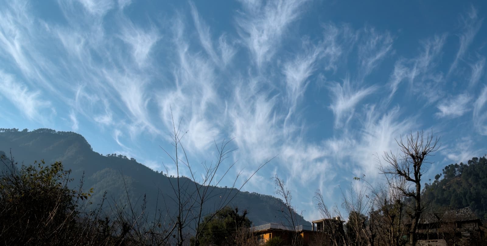 Wispy white clouds against a blue sky. A tree-lined hill rises up against the sky.