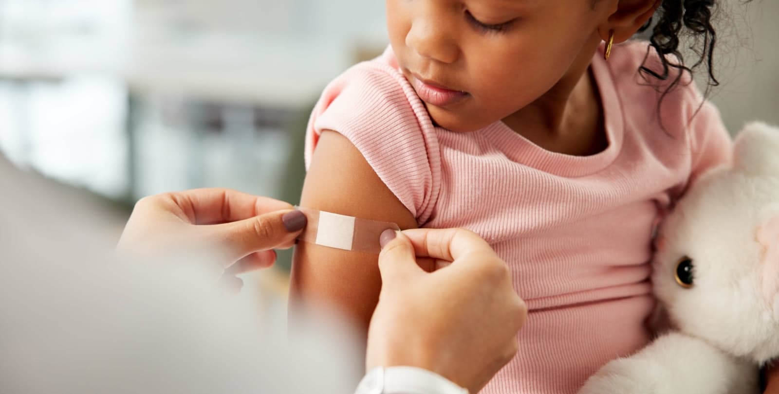 A doctor places a bandaid on a girl's arm after a vaccine.