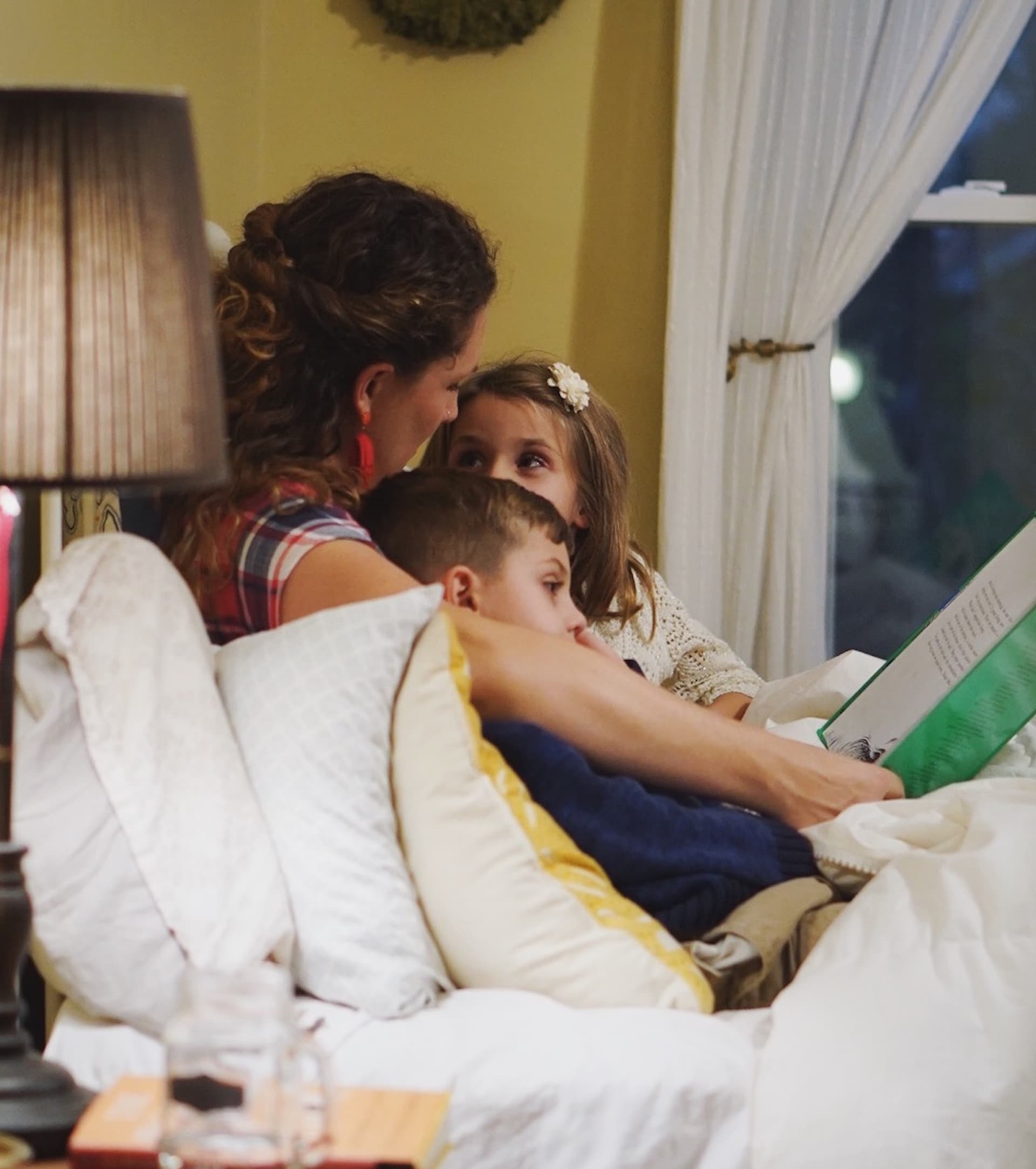 a mother reading a book to two children on a bed