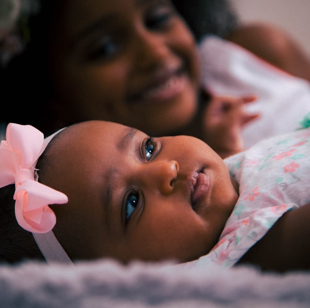 baby in headband with older sibling looking on