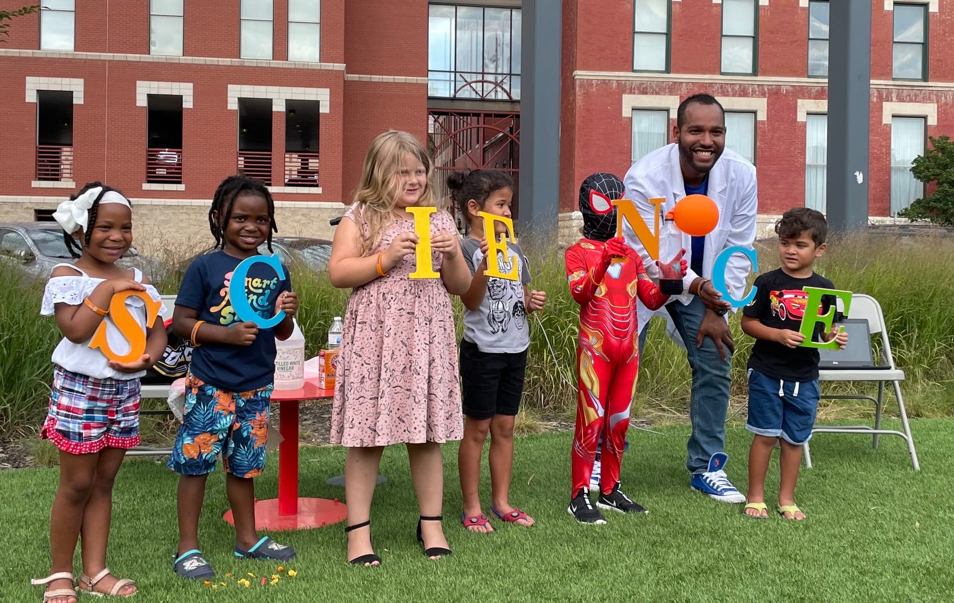 Roy standing with kids holding individual letters of the word Science